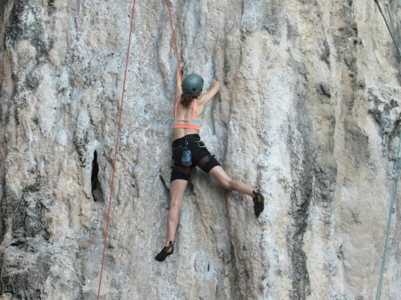 Woman climbing a limestone cliff with ropes. Outdoor sport showcasing strength and adventure.