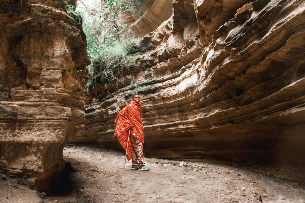 A man wrapped in a red blanket standing in an eroded sandstone canyon, showcasing natural beauty.